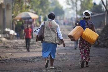 Noella pictured carrying water containers while walking next to a mercy corps program officer
