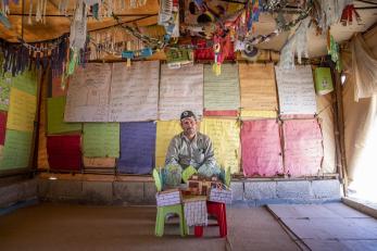 Ahmad sitting behind his model house, inside the school in front of a colorful wall