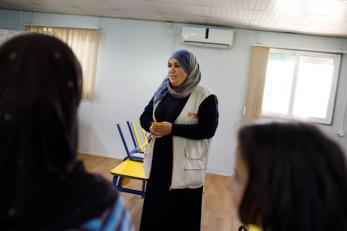 Eman with her hands folded in front of her wearing a mercy corps vest and headscarf