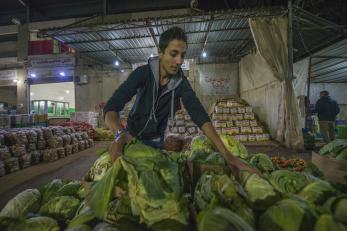 Man in hooded sweatshirt displaying lettuce at a market