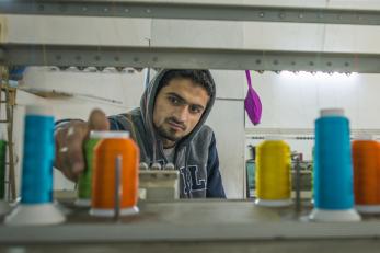 Bashar next to a machine with large spools of colorful thread