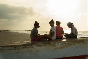 Four youth sitting at the beach with sun behind them