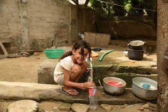 Girl smiling, crouching to fill a water bottle