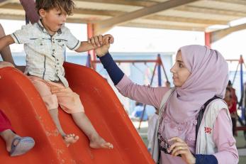 Woman in jordan holding the hand of a boy seated at the top of a slide