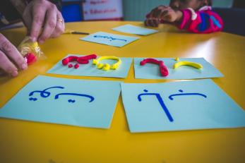 Malak rolls and shapes clay to trace letters on cards