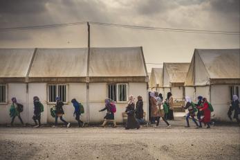 People walk with backpacks by buildings with canvas roofs