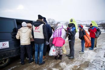 Mercy corps staff help a group of refugees into a van that will help transport them to the next stop on their journey.