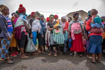 A group of women gathered with bundles of clothing. several women are holding babies.