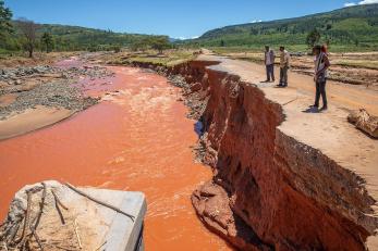 Three mercy corps employees next to a clay colored river impacted by flooding