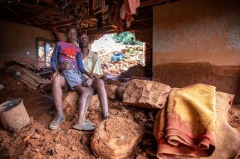 A man with his son sitting on his lap, pictured in a building surrounded by rubble