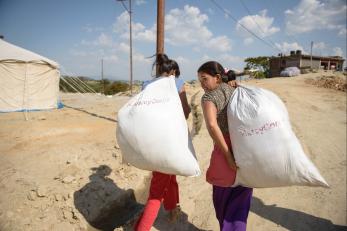 Two young women carrying large mercy corps bags of supplies