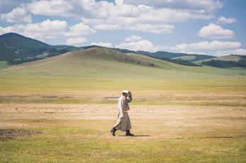 Man in long jacket and hat walking through empty field