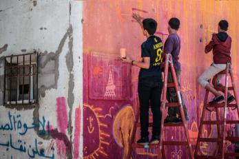 Yousef and two other boys on ladders painting a mural