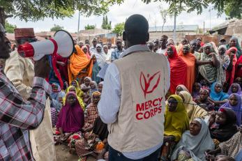 Man in mercy corps vest faces away from camera toward a crowd of people