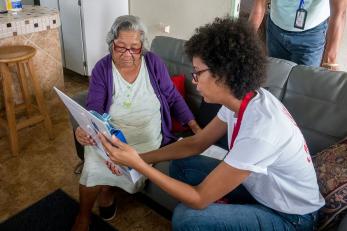 A mercy corps employee sitting with an older woman, both looking at a clipboard