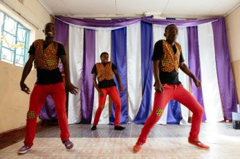 Young people in matching red pants, black shirts and patterned vests performing a dance