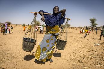 A woman balancing two buckets across her shoulders on a stick