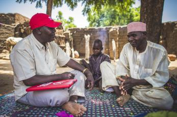 A mercy corps employee, left, talking with alhaj, who is with a young boy.