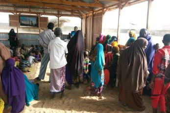 People sitting and standing in a shelter watching a movie that is being played