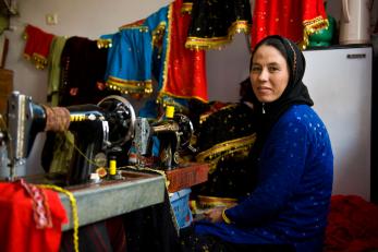 Woman at sewing machine with colorful cloth draped in background