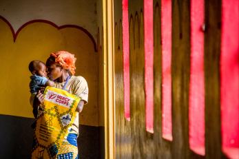 A woman holding her son in front of a yellow mural