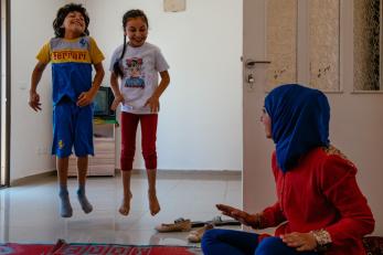 Suzanne seated on the floor with two of her children jumping in the background