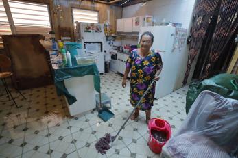 Carmen stands in her kitchen with a mop and bucket