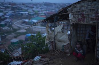 Small girl crouching outside shelter above camp