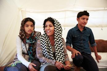 A woman, girl and boy pictured sitting together inside a white canvas tent