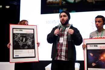 A man on stage with a microphone presenting his photograph, difference, which is being held up by the woman next to him.