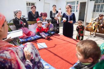 Women and children seated around a room with a red carpet in the center