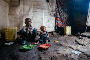 A boy and toddler with two plates of food in front of them, sitting on the floor of their home