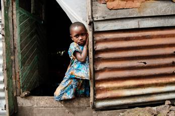 A child standing on a stoop with hands pressed against side of doorway