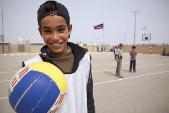 A teenage boy holding a ball and smiling in a refugee camp in jordan
