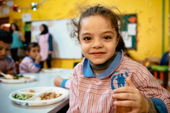 A girl with a plate of food in front of her on the table at school in lebanon