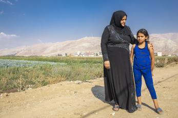 Woman and child stand next to agricultural field.