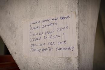 Image: a message on notebook paper reads "please wash your hands before entering. join us fight ebola. ebola is real! save your self, your family and the community.