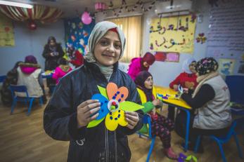 Girl in a classroom in jordan, holding a craft project and smiling