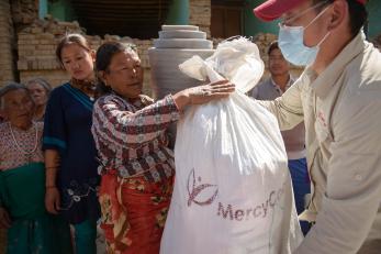 Woman receives a bag of supplies labeled with the mercy corps logo in nepal