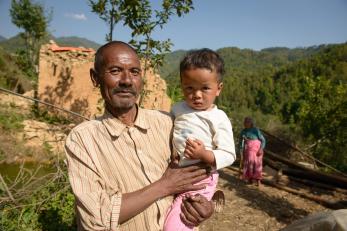 Man holding a young child in nepal with green forested hillside in background