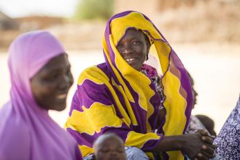 A woman smiles while leading a savings group in niger. she is wearing yellow and purple