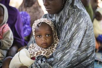 A toddler looking up, wrapped in her mother's arms