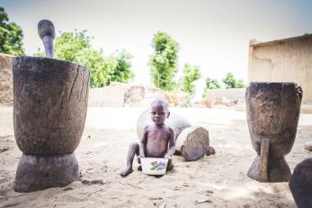 A young boy sitting with a white basin in front of him. there is a peacock design on the basin and a serious expression on his face.