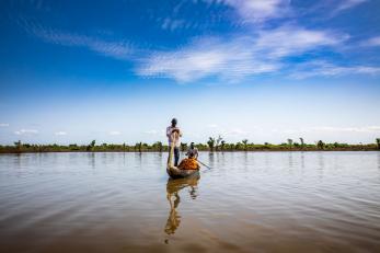 Fishermen paddle a small wooden boat in nigeria. the man at the bow is standing.