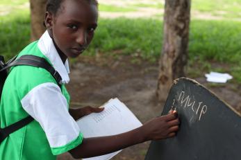 A girl in south sudan writes on a chalkboard outdoors