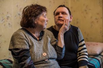 A elderly women rests a hand gently on the cheek of her adult son, who has a disability