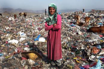 A woman in yemen standing among trash with cows in the background