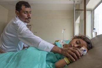 Abdullah checks on his daughter, who is lying in a hospital bed