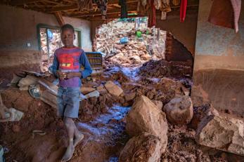 A boy walks barefoot through a home filled with rubble