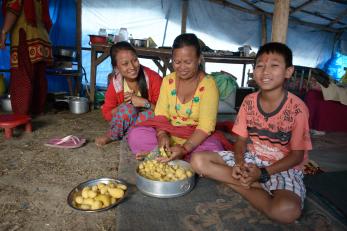 A woman in nepal prepares potatoes while her daughter and son sit nearby
